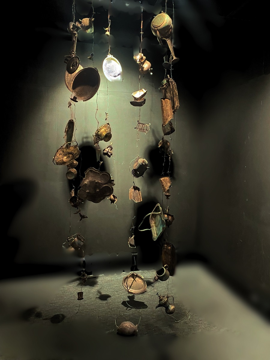 The image shows a collection of various found vintage objects hanging in mid-air against a dark background. These objects include vintage silverware, nickel silver barbed wire with a patina. A light source from above casts dramatic shadows, creating a sense of depth. The arrangement is balanced and artistic, with each object placed at different heights and distances, giving the scene a ghostly look.